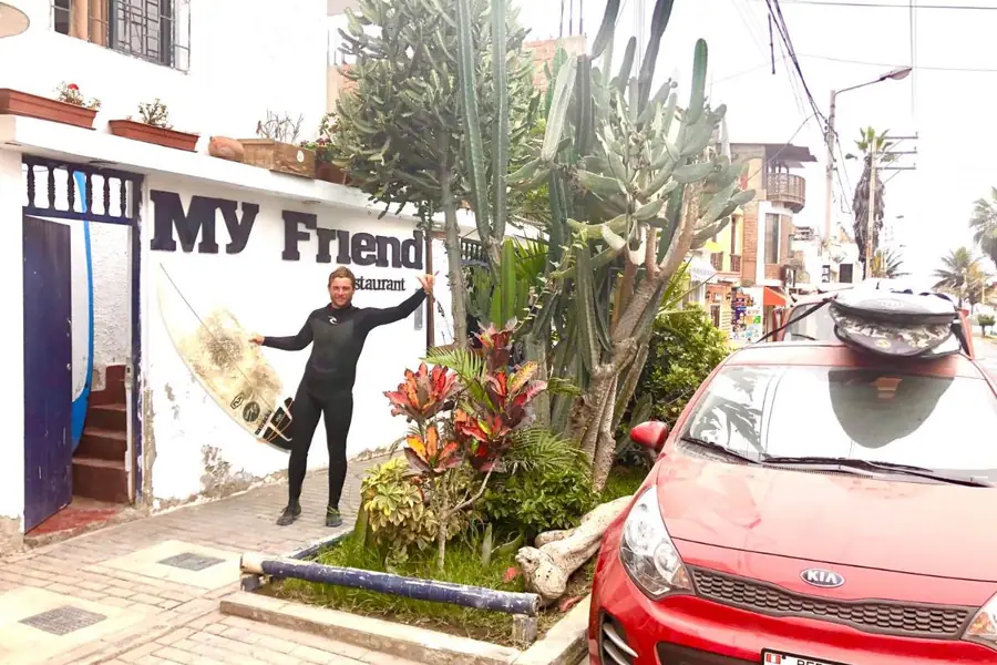 The entrance to My Friend Surf Hostal with its sign and a surfer carrying a board, in Huanchaco